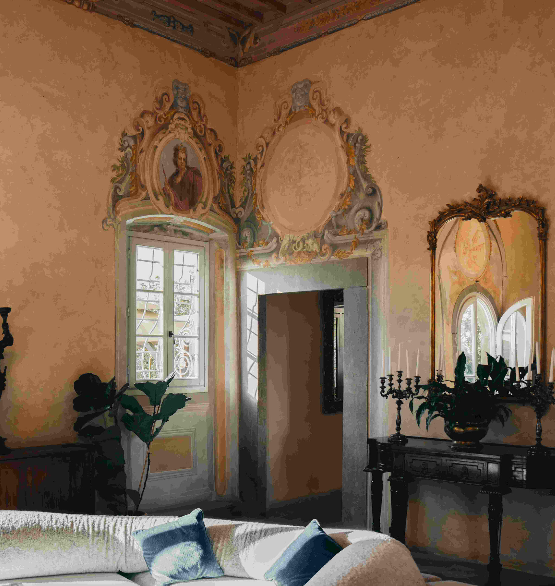 An elegant living room featuring frescoed walls with detailed moldings, a wooden beamed ceiling, and antique decorative elements in a house rented by a customer in Tuscany.