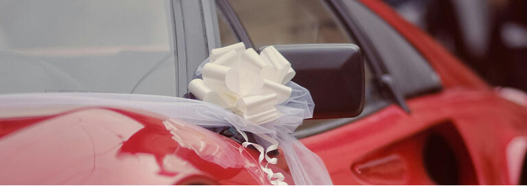 Close-up of a glossy red sports car decorated with a large white wedding bow for a wedding in Florence, Italy.