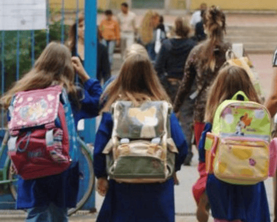 A group of children walking together on a sunny day, smiling and chatting as they go to school in Tuscany, Italy.