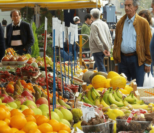 A group of people interact around a fruit stand at a Florence market filled with an assortment of fresh fruit, enjoying the market atmosphere, which is one of the nuances of everyday life in Tuscany.